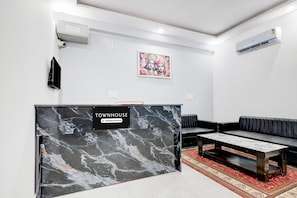 Un espace d’accueil doté d’un comptoir en marbre, d’un canapé en cuir noir et d’un tapis à motifs rouges.