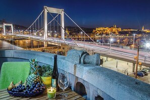 Een balkon met een eettafel, met uitzicht op een brug en een stadsbeeld 's nachts.
