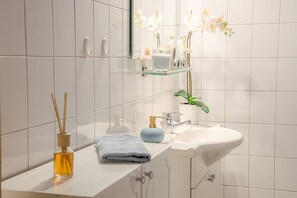 Een moderne badkamer met een witte wasbak, een blauwe zeepbakje, een glazen kandelaar en een kleine plant in een pot.