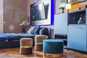 Een moderne slaapkamer met een bed, twee voetenbankjes, een televisie en een lamp.