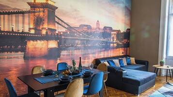 A dining area with a mural of a bridge, a table set for two, and a sofa.