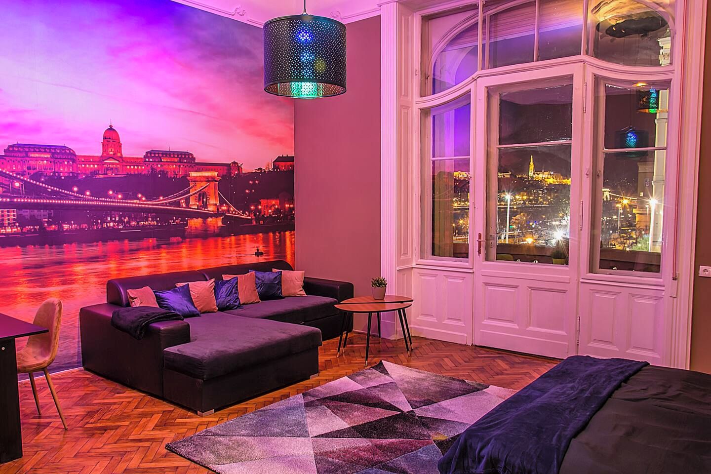 A room with a large window, a sofa, a small table, and a chair.