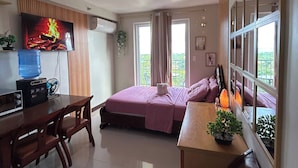 Ein Zimmer mit einem Bett, einem Schreibtisch, einem Fernseher, einem Wasserspender und einem Fenster mit Vorhängen.