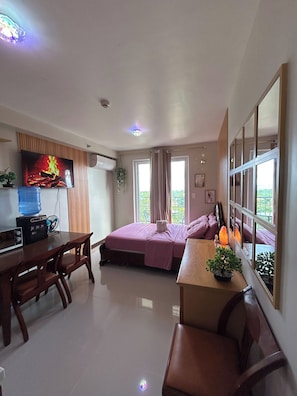 A room with a bed, a desk, a TV, a water dispenser, and a window with curtains. - Budget Friendly-seaview w Balcony Near Airport (Lapu-Lapu)
