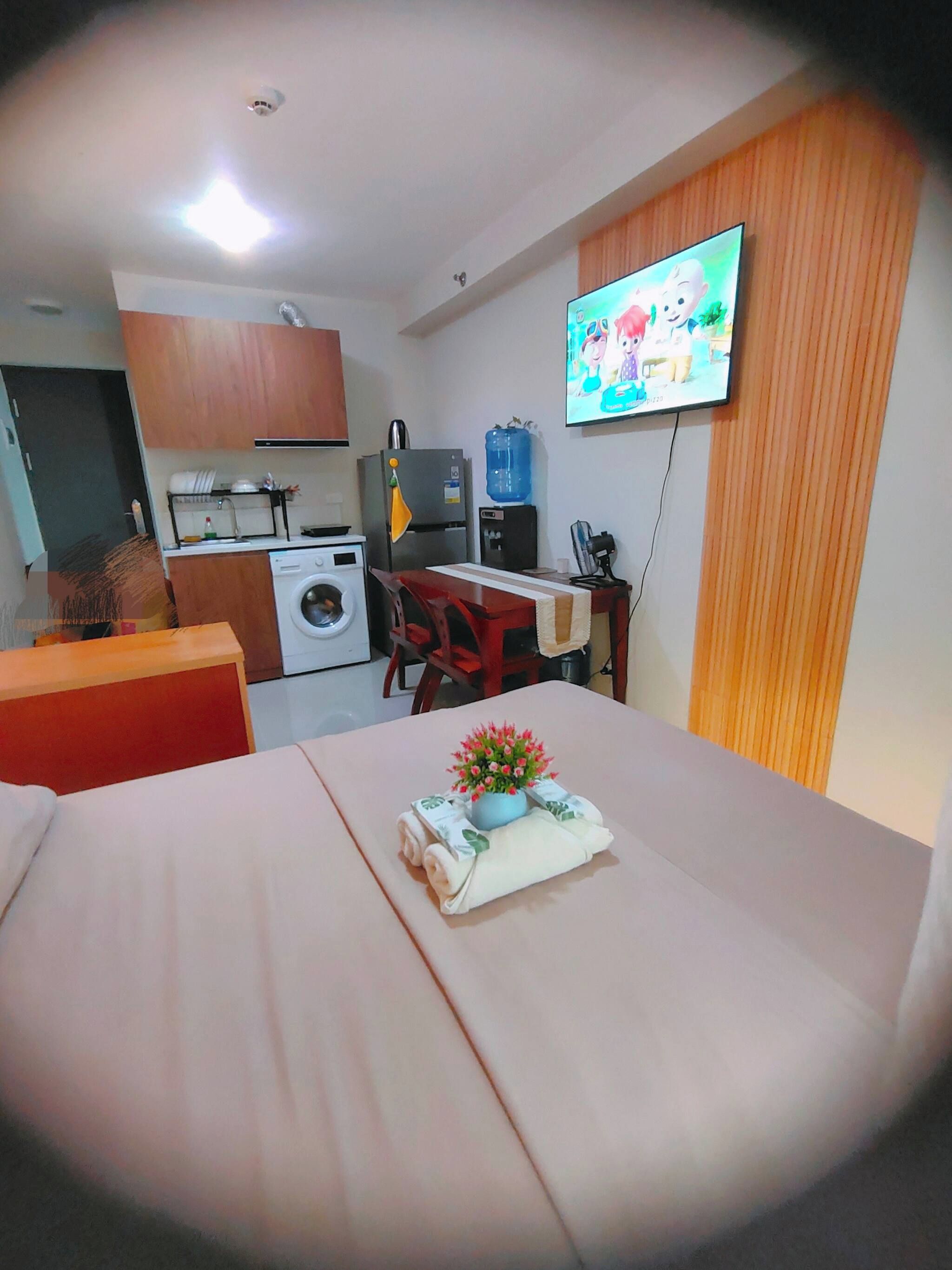 Habitación de hotel compacta con cama, kitchenette pequeña, lavadora y televisión.