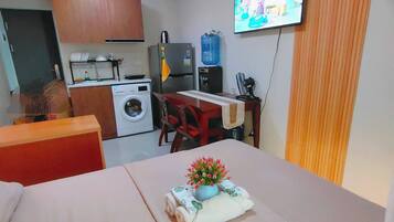 Habitación de hotel compacta con cama, kitchenette pequeña, lavadora y televisión.