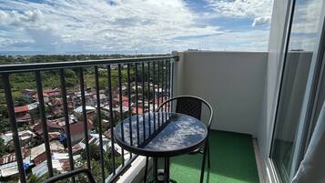 A balcony with a glass table and two chairs, overlooking a residential area with houses and greenery.