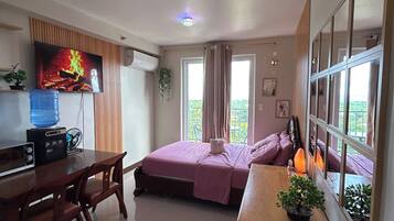 Una habitación con cama, escritorio, silla, dispensador de agua y televisor.