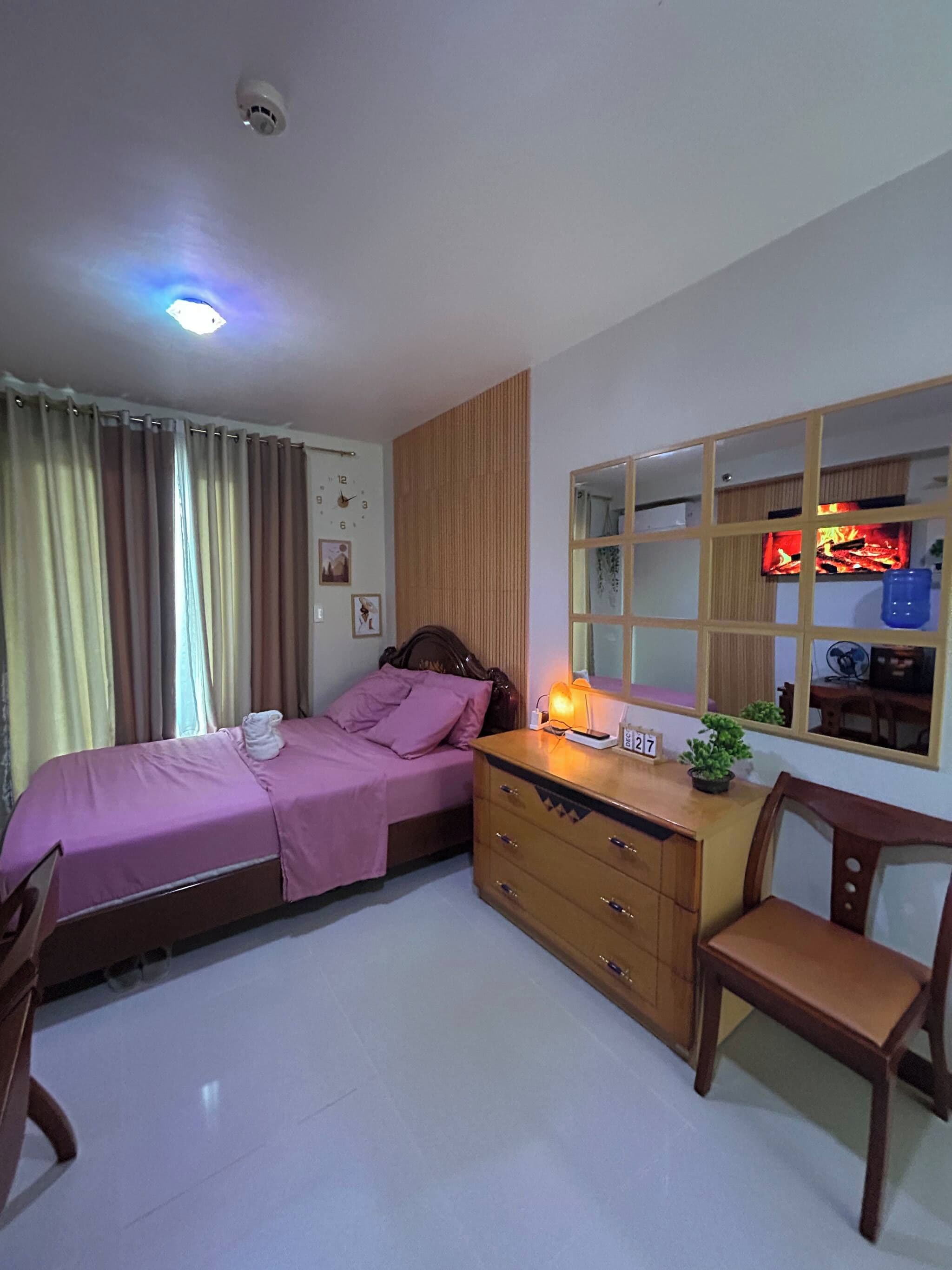 Un dormitorio con cama, cómoda, silla, ventana y reloj de pared.