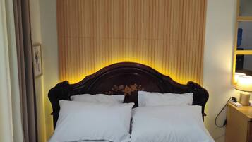 A hotel room with a bed, pillows, a headboard, a nightstand with a lamp, and a wall with vertical lines.