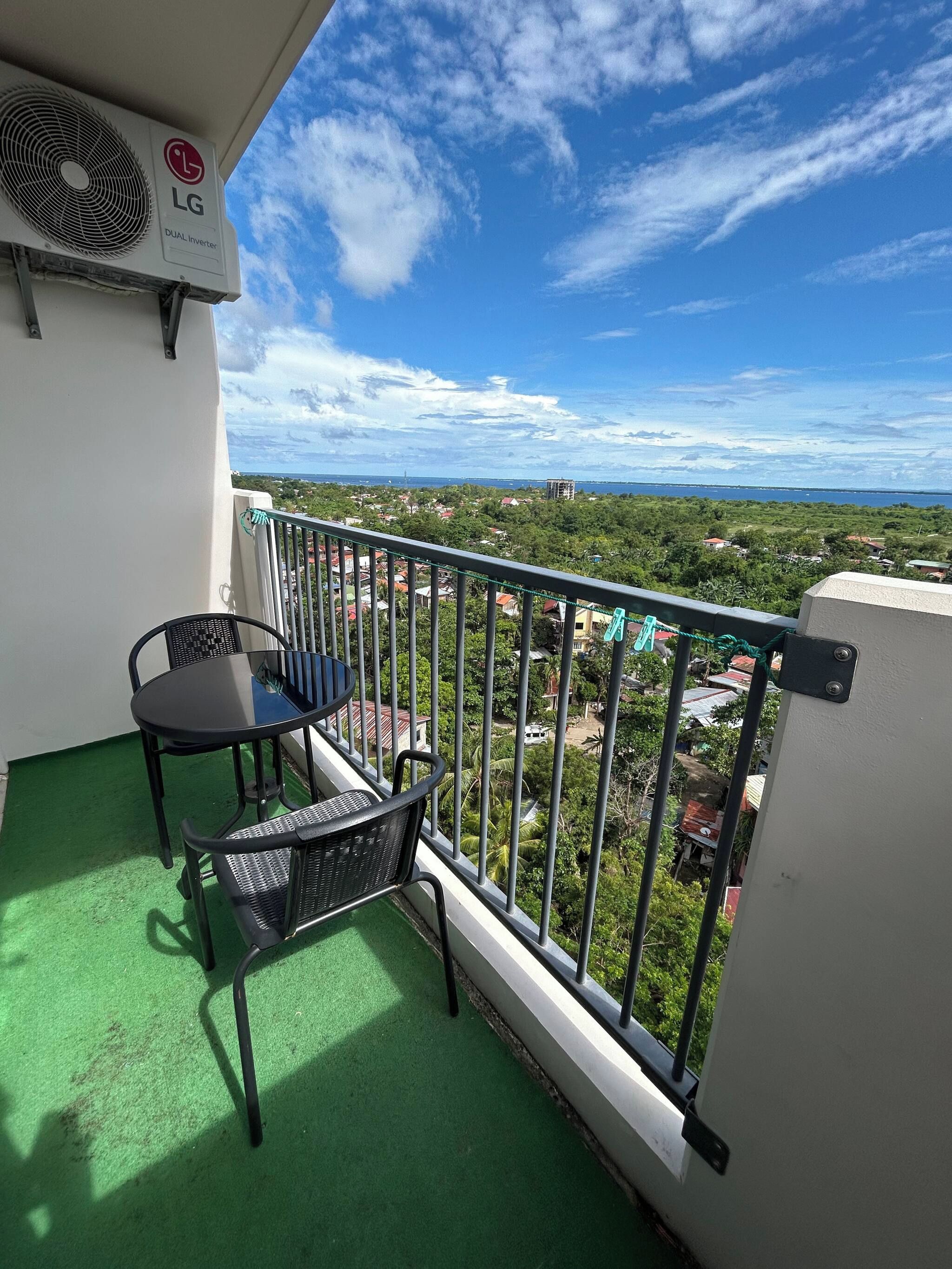 A balcony with a table and chairs, a view of a coastal area, and an LG dual inverter air conditioning unit.
