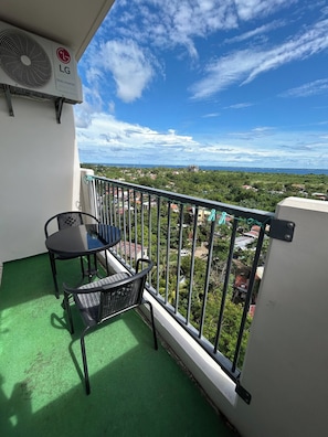 A balcony with a table and chairs, a view of a coastal area, and an LG dual inverter air conditioning unit. - Budget Friendly-seaview w Balcony Near Airport (Lapu-Lapu)