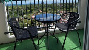 Ein Balkon mit rundem Tisch und zwei Stühlen mit Blick auf eine Stadtlandschaft aus Gebäuden und Grünflächen.