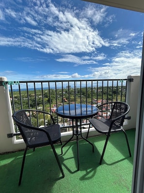 A balcony with a round table and two chairs, overlooking a cityscape with buildings and greenery. - Budget Friendly-seaview w Balcony Near Airport (Lapu-Lapu)