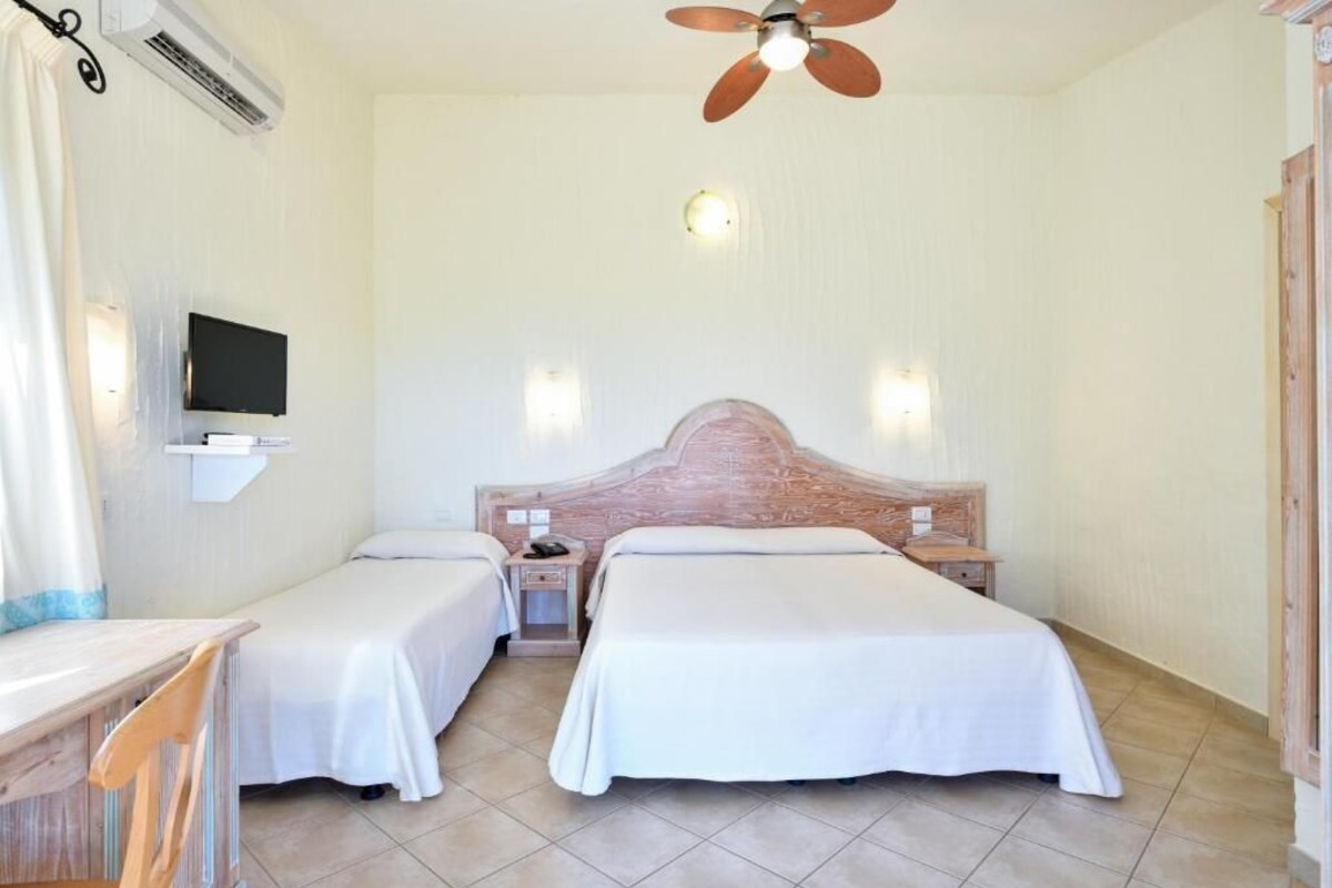 Hotellihuone, jossa on kaksi sänkyä, työpöytä, tuoli, televisio ja kattotuuletin.