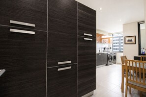 Eine moderne Küche mit dunklen Schränken, ein Essbereich mit einem Holztisch und Blick auf die Stadt durch große Fenster.