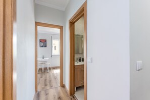 Um corredor com porta de madeira, parede branca e uma pequena mesa com cadeiras.