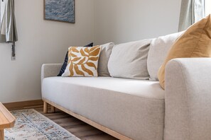 A neutral-colored sofa with patterned cushions, a wooden floor, and a simple wall with a single piece of wall art. - Nomad's Family - 2-Bedroom Apartment at The Docks in Porto (Porto)