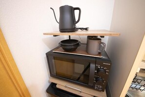 A compact kitchen setup with a microwave, a kettle, and a mug on a shelf. - goom Monthly Nakasu Maxim (Fukuoka City Chuo-ku Haruyoshi)