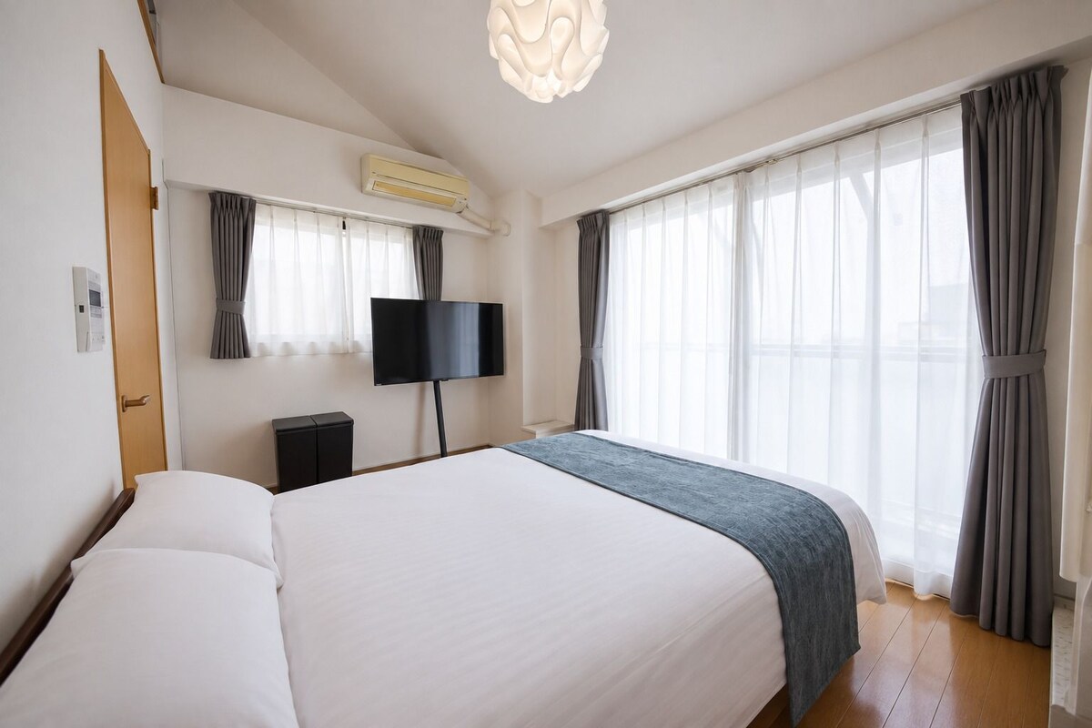 A hotel room with a large bed, a flat-screen TV, a ceiling light fixture, and a window with curtains.