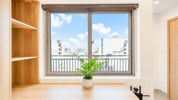 Una habitación con ventana, una planta en maceta, una mesa de madera y una silla.