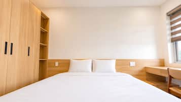 A hotel room with a large bed, wooden wardrobe, and a desk with a chair.