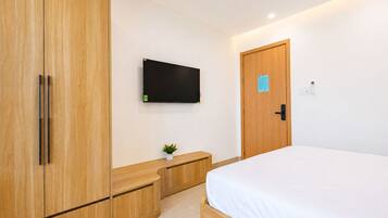 A bedroom with a bed, wooden wardrobe, a small plant, a flat-screen TV, and a door with a lock.