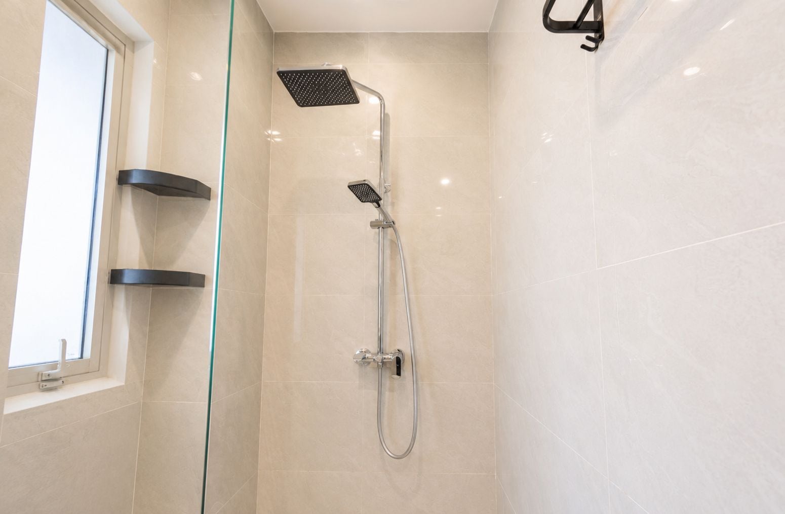 A modern bathroom with a glass shower enclosure, a handheld showerhead, and a wall-mounted faucet.