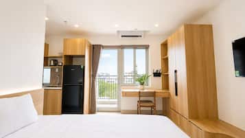 Habitación de hotel con cama, escritorio, refrigerador, planta en maceta y ventana con vista a la ciudad.