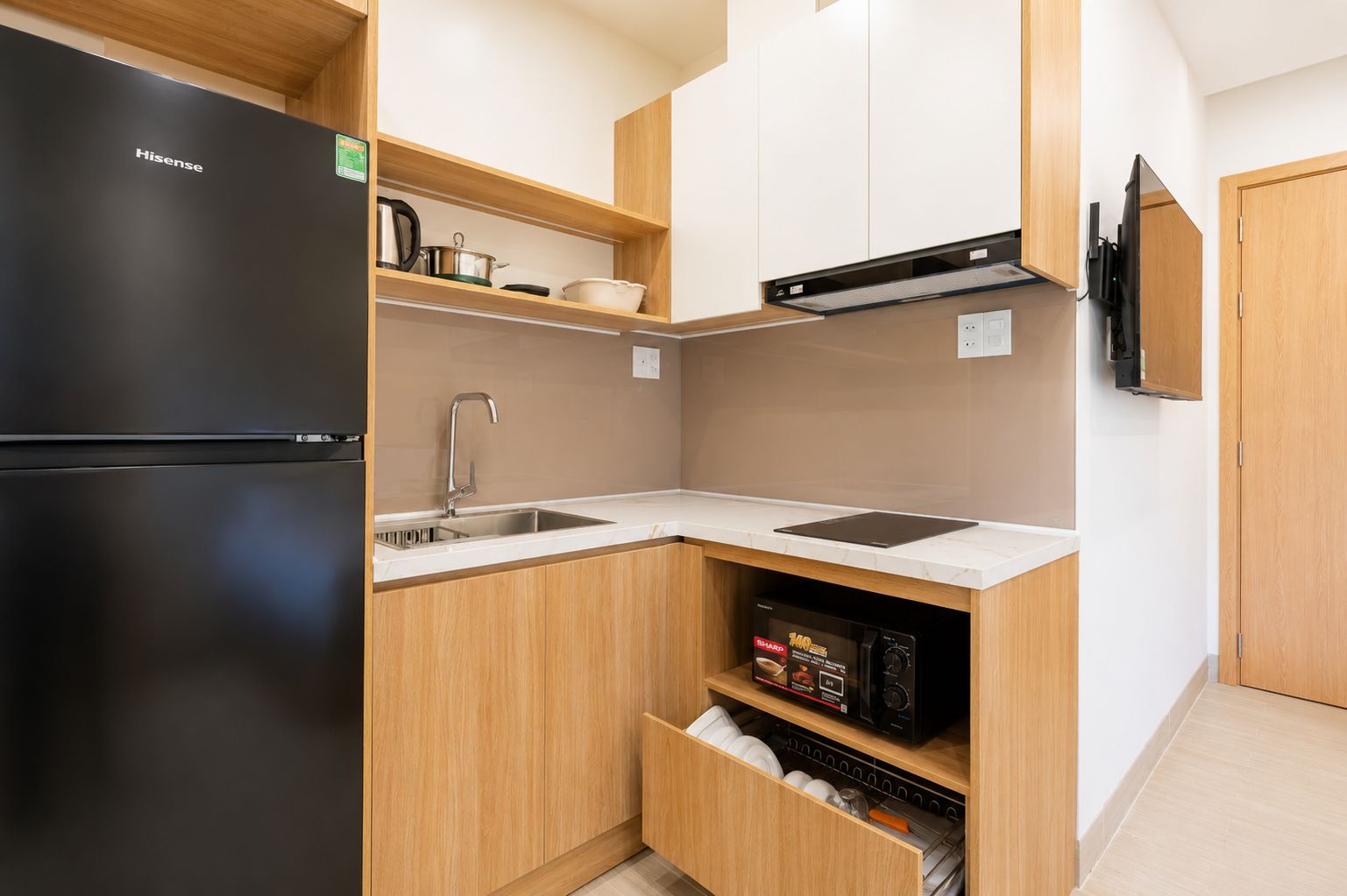 Una cocina compacta con un refrigerador negro, un lavamanos, armarios de madera y un microondas.