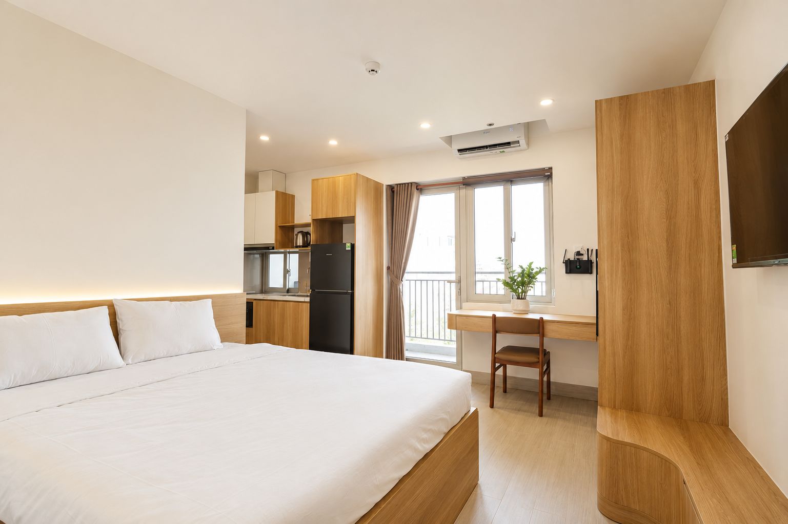 A hotel room with a bed, a desk, a kitchenette, and a balcony.