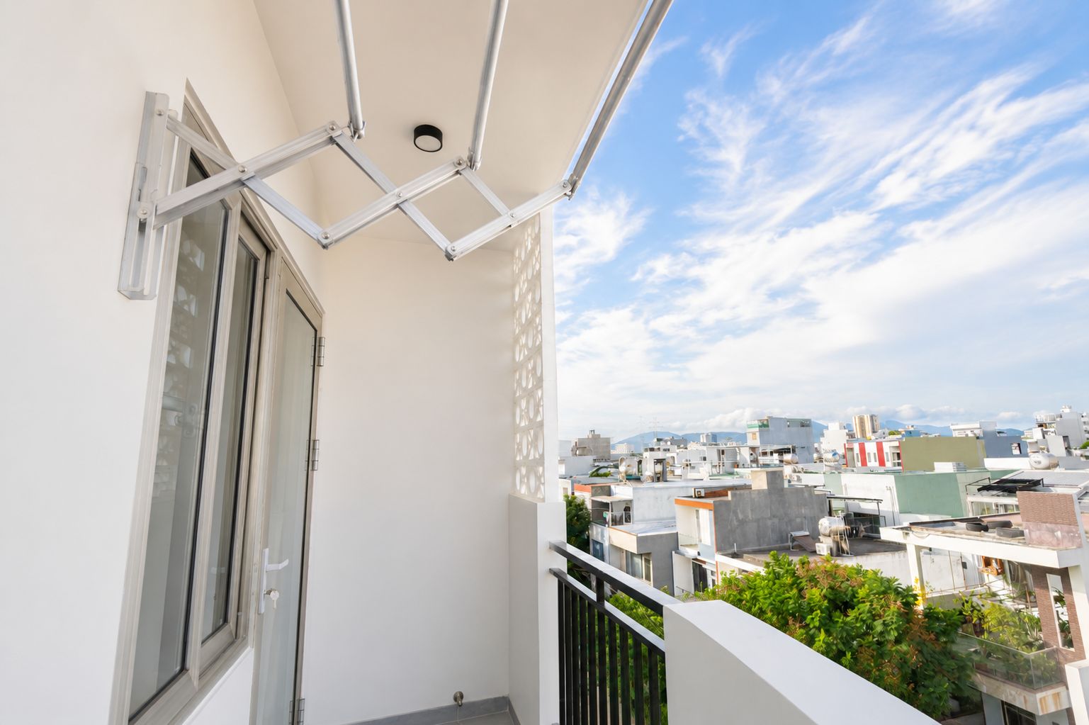 A balcony with a view of a cityscape, a window, and a metal structure.