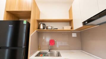 A compact kitchen with a black refrigerator, wooden cabinets, a marble countertop, and a stainless steel sink.