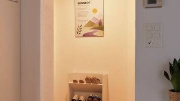 Ein Flur mit Holzboden, einem Schuhregal, einem Poster und einem Thermostat an der Wand.