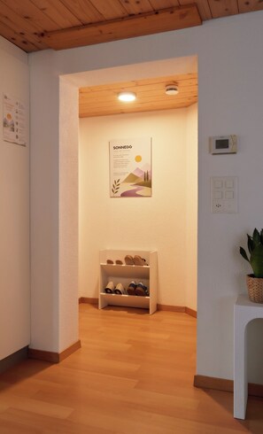 A hallway with a wooden ceiling, a shoe rack, a poster, and a thermostat on the wall.