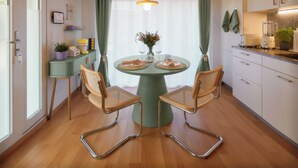 Ein Essbereich mit einem runden Tisch, zwei Stühlen, einer Blumenvase und einer Küche im Hintergrund.
