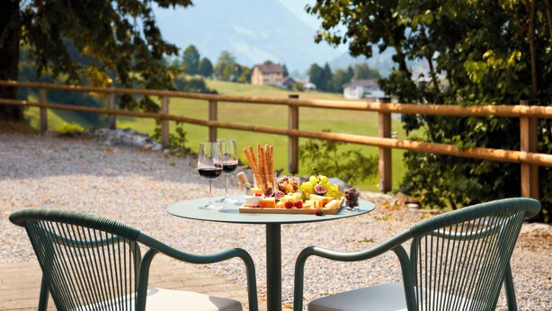 Ein Tisch mit einer Käseplatte, Weingläsern und Blick auf eine Berglandschaft.