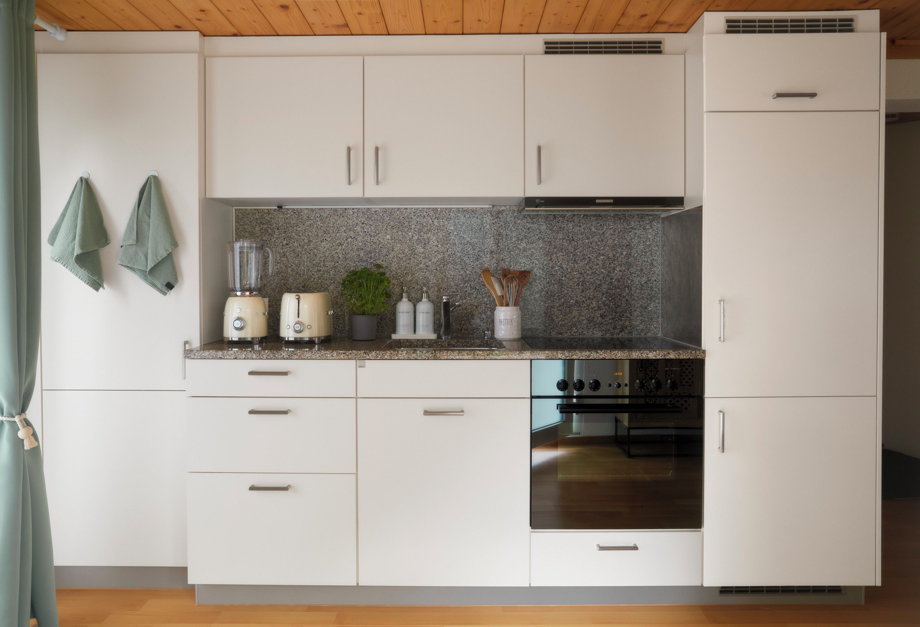 Eine Küche mit weißen Schränken, einer Granit-Arbeitsplatte, einem Mixer, einem Toaster, einem Herd und einem Kühlschrank.