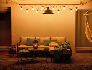 A cozy living room with a sofa, pillows, a small round table, and a hanging light fixture.