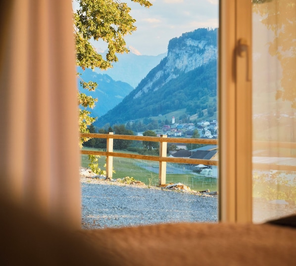 A window view of a mountainous landscape with a wooden fence in the foreground.