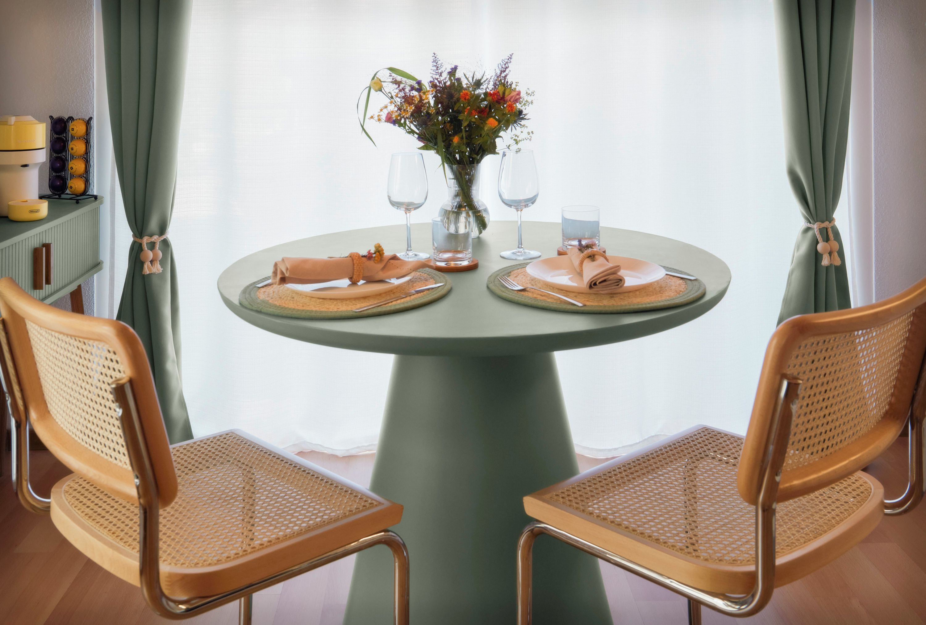 Ein runder Tisch mit zwei Stühlen, einer Vase mit Blumen und zwei Weingläsern.
