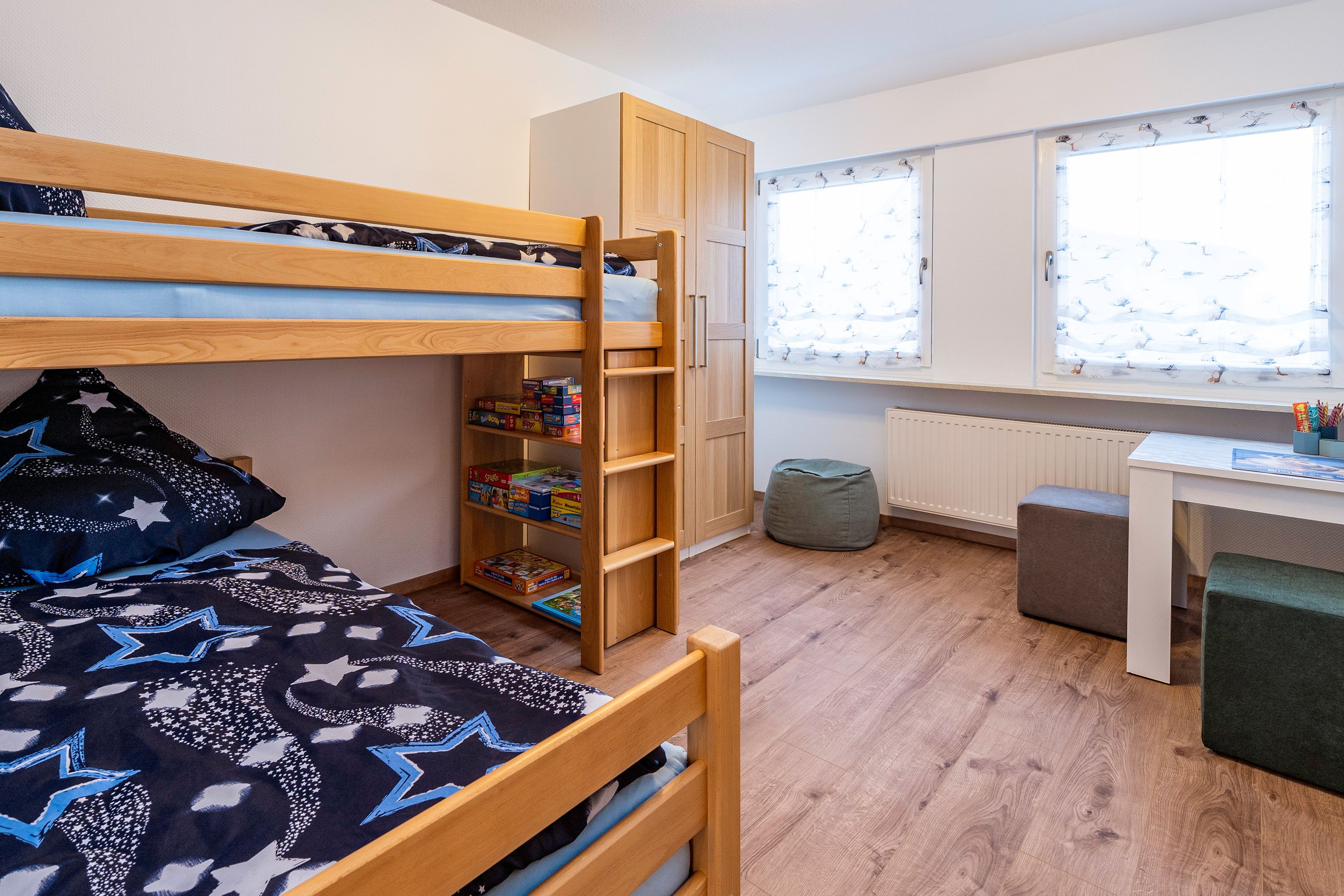 Een stapelbed met een kastenonderstel, een bureau met stoel, en een radiator.