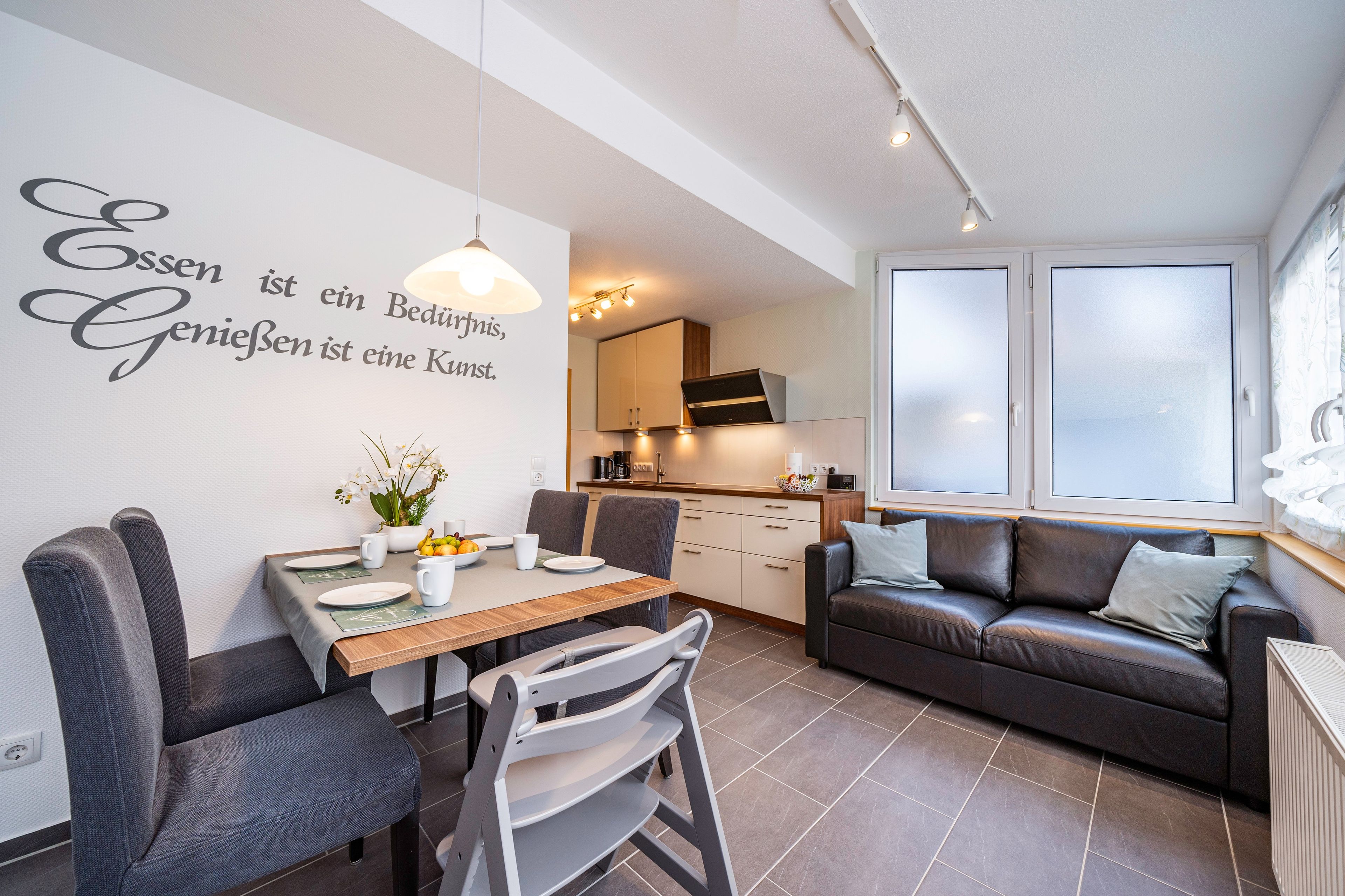 Ein modernes Wohnzimmer mit Essbereich, einer Couch und einer Küche im Hintergrund.