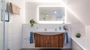 Une salle de bain moderne avec un grand miroir, un meuble-lavabo en bois et une petite plante en pot.