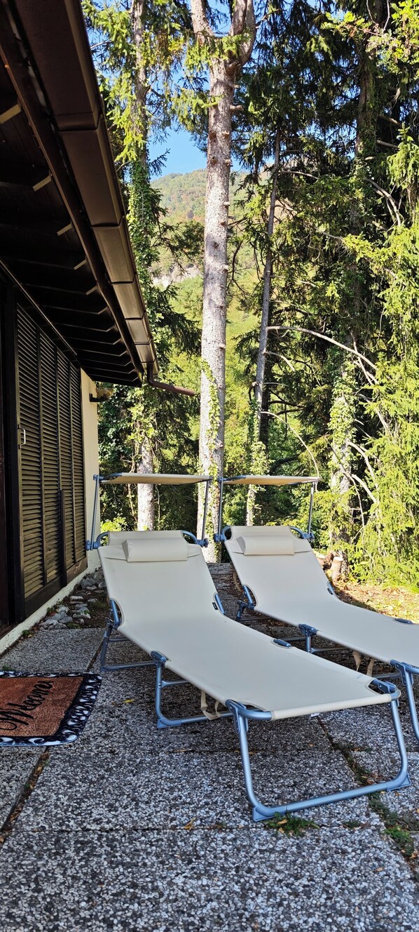 Deux chaises longues dotées d’une structure en métal et de coussins beige, placées sur une surface de gravier, avec une terrasse en bois et une rambarde en métal en arrière-plan.