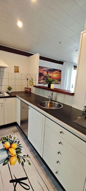 A kitchen with a sink, cabinets, and a window with a view of a sunset. - Idyllic Bungalow with Lake View & Pool in Tignale (Aer)
