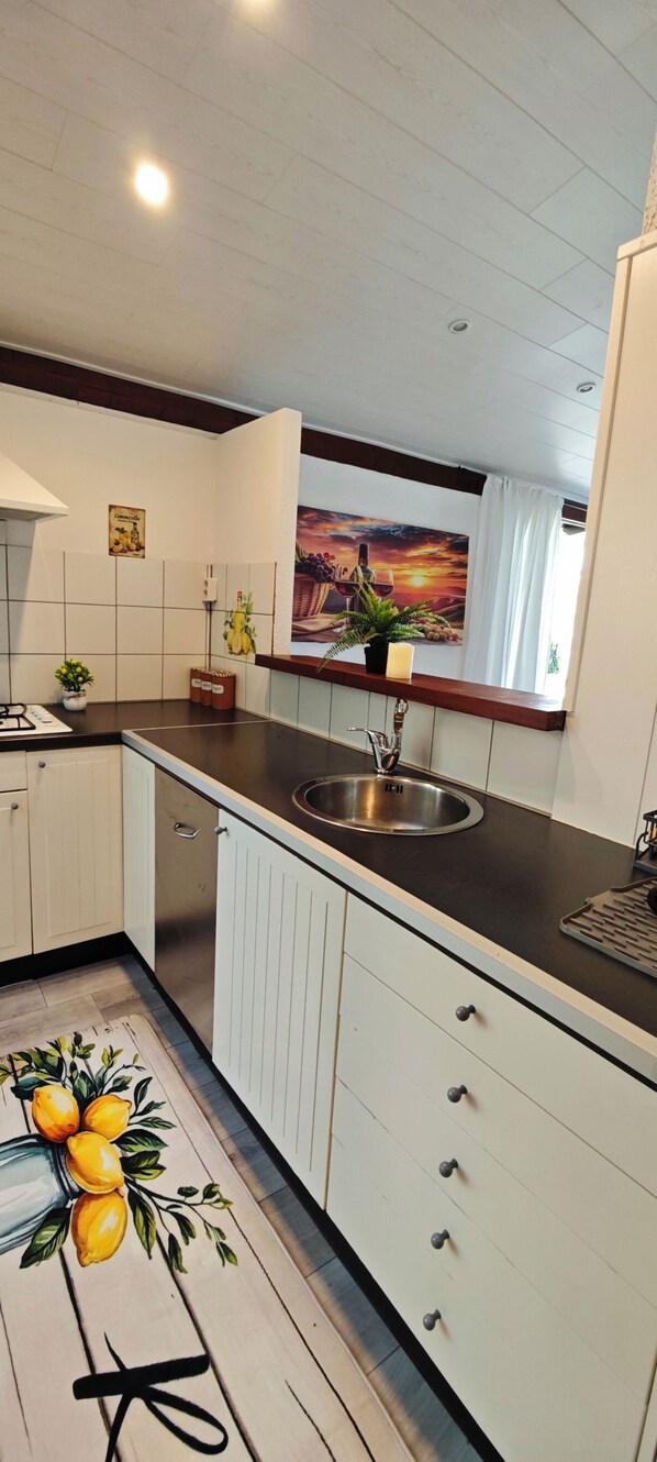 A kitchen with a sink, cabinets, and a window with a view of a sunset. - Idyllic Bungalow with Lake View & Pool in Tignale (Aer)
