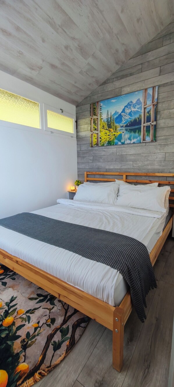 A bedroom with a wooden bed, a painting of a mountain landscape, and a window with frosted glass. - Idyllic Bungalow with Lake View & Pool in Tignale (Aer)