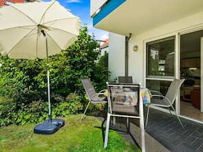 Eine Terrasse mit Tisch und Stühlen, einem weißen Sonnenschirm und einem Rasen.