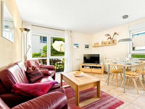 Ein Wohnzimmer mit einer Ledersofa, einem Holztisch, einem Fernseher auf einem Holzständer und einem Essbereich mit Stühlen und Tisch.